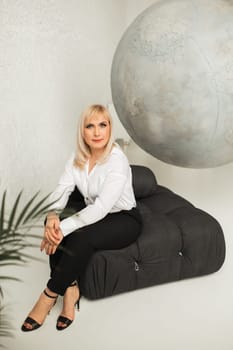 A fashionable woman In a white shirt and black pants poses in the interior