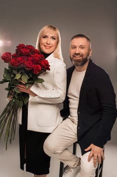 A man and a woman with flowers in their hands in strict clothes pose in the background in the studio