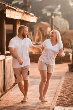 A happy married couple in shorts and T-shirts walks down the street at sunset in summer