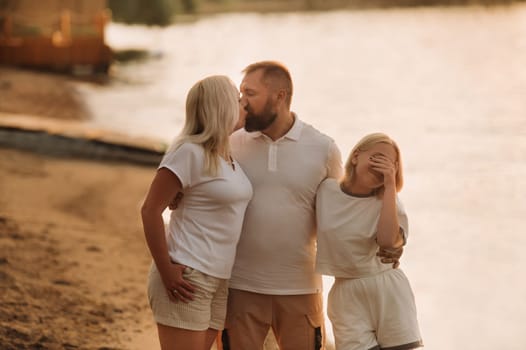 Happy family - father, mother and daughter in light clothes having fun together on the beach in summer