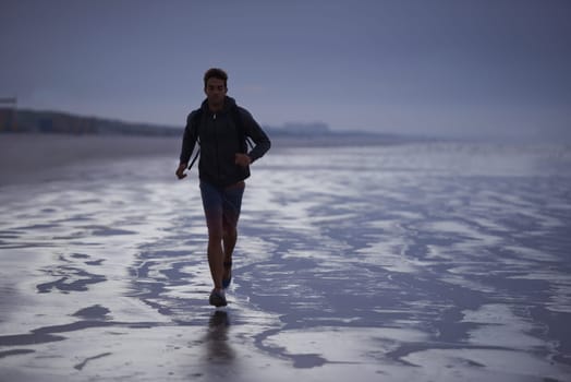 Starting the day with a jog on the beach. A young man jogging on the beach in the early morning.