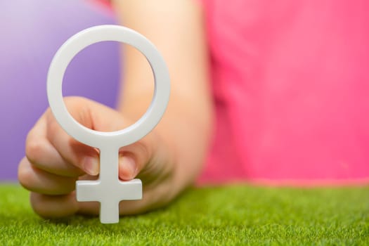 The concept of gender. Female gender symbol in hand on purple background in pink t-shirt with copy space