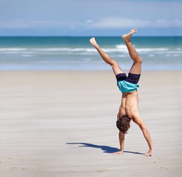 Who can make the longest hand stand. Young man doing a hand stand on the beach.