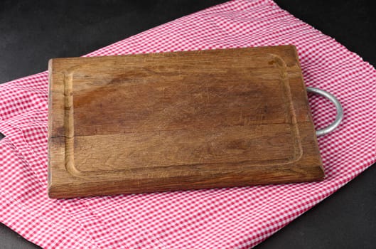 Empty wooden cutting board and red towel on black background. Copy space