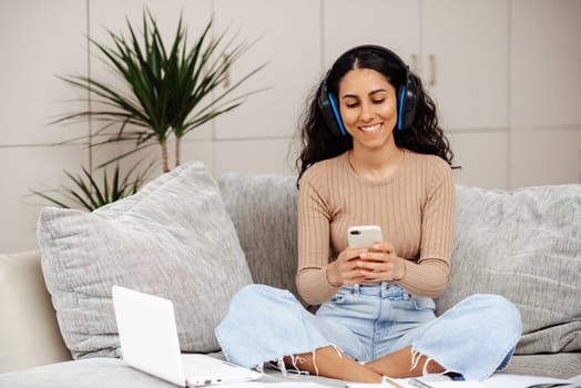 Arab girl teen enjoy learn MBA class study at home relaxed sit sofa work read text in social media, scroll laptop search app, watch wifi movie. Blogger girl smile happy life listen music multi task.