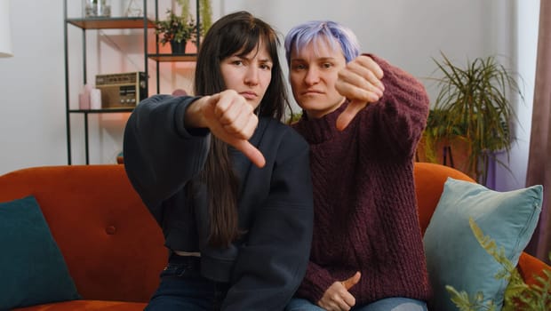Upset lesbian women family couple showing thumbs down sign gesture expressing discontent disapproval