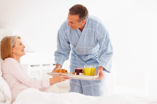 Caring mature man serving breakfast to his wife in bed. Portrait of caring mature man serving breakfast to his wife in bed.