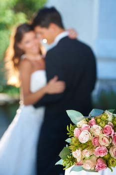 Flowers for the reception. embracing newlyweds with focus on a bouquet in the foreground.