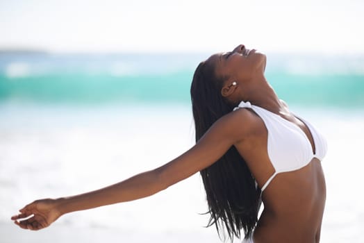 Refreshed by the sea breeze. An african-american woman with her arms outstretched and eyes closed at the beach.