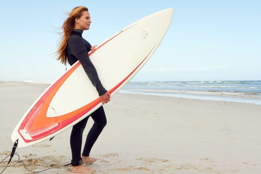 Ready to hit the waves. a female surfer standing on the beach with her surfboard.