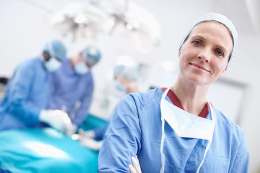 Time is life, not money in this business. Angled portrait of a mature female surgeon wearing hospital scrubs with her work colleagues in the background operating.