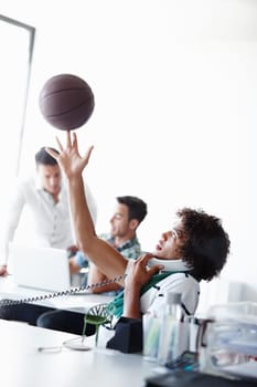 He cant wait to get to basketball. A young man playing with a basketball while sitting in the office.
