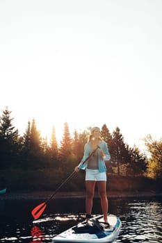 Nature is a place you never grow tired of. a young woman paddle boarding on a lake.