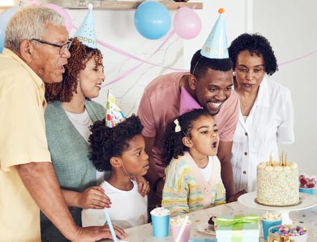 Birthday, cake and a girl blowing out candles while celebrating with her black family in their home. Kids, party or celebration with parents, grandparents and children bonding together in a house.