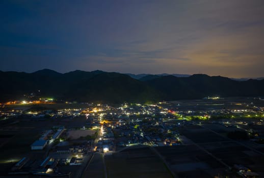Lights from houses and streets in small town at foot of mountain range at twilight