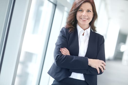 Portrait of a confident businesswoman or lawyer standing with her arms crossed in an office. One happy business professional smiling standing with arms folded at work. Manager at a successful company