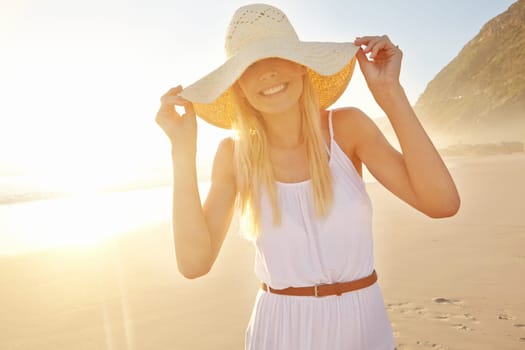 Enjoying a beautiful day. a gorgeous young woman wearing a white dress and sunhat on the beach.