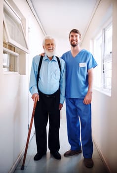 Were in this together. a young doctor helping his senior patient walk down a hallway in hospital.