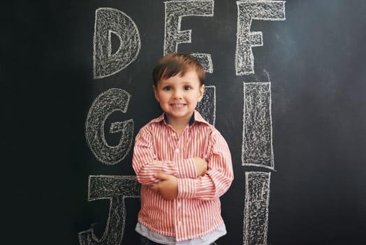 Learning the ABCs. A little boy standing in front of a blackboard with letters written on it.
