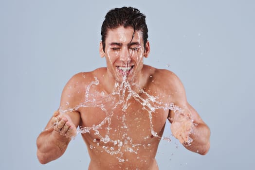 Splish splash. Studio shot of a bare-chested young man splashing water on his face.