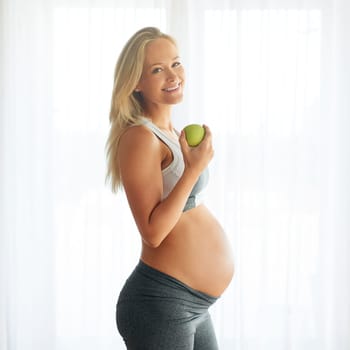 Some call it healthy eating, I call it love. Portrait of a happy pregnant woman dressed in sportswear and eating an apple at home.