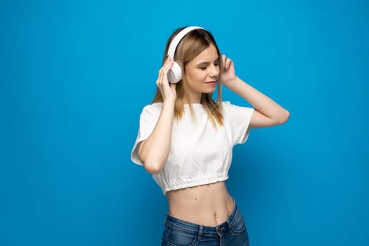 Young blonde woman with headphones listening music .Music teenager girl dancing against isolated blue background.