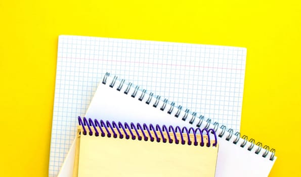 White and beige notepads and a checkered notebook on a yellow background. 