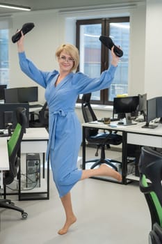 Caucasian business woman stands barefoot with shoes in her hands among the office.