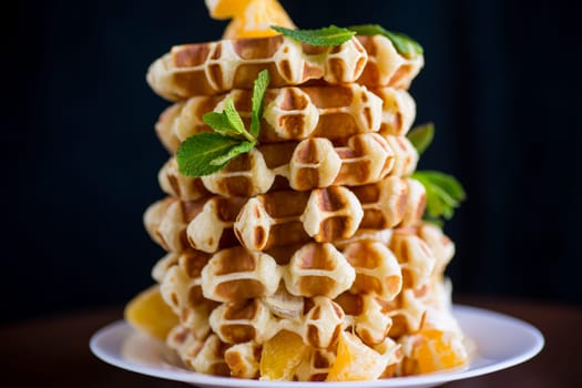Cooked sweet Belgian waffles with oranges on a black