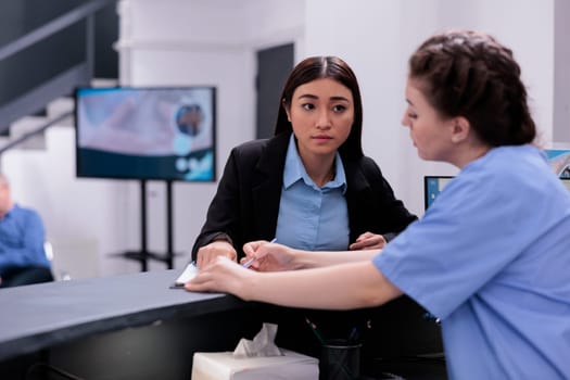 Nurse showing medical report to receptionist discussing expertise during checkup visit examination