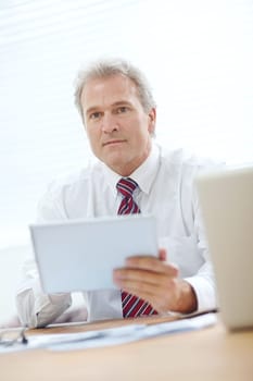 Considering further information. Head and shoulders shot of a mature employee holding a tablet while looking away from the camera.