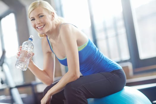 Water has never tasted this good. an attractive young woman laughing and holding a bottle of water while sitting on a pilates ball at gym.