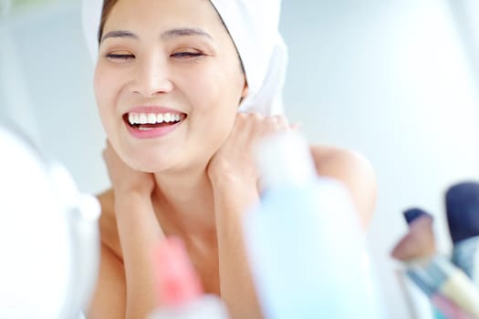 Happy with her beauty routine. A beautiful young Asian woman smiling while sitting in her bathroom with a towel on her head.