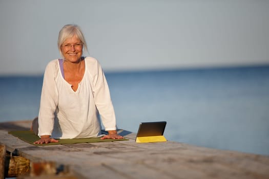Finding yoga instructions online. A mature woman doing yoga exercises on a pier with the help of her digital tablet