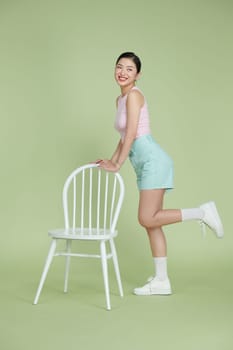 Full length of a smiling young pin up woman standing near chair and looking at camera