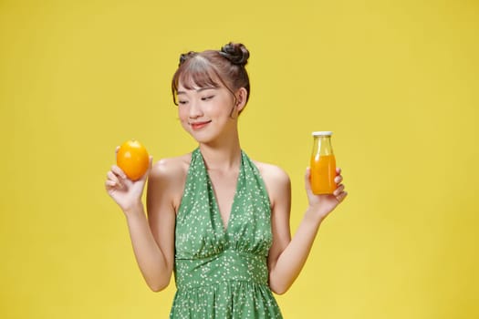 Portrait image of a young woman holding an orange and a glass of fresh orange juice