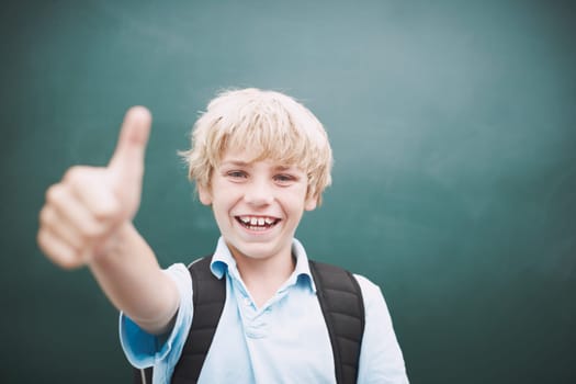 I love learning. A young boy giving you a thumbs up against a blackboard in his classroom.