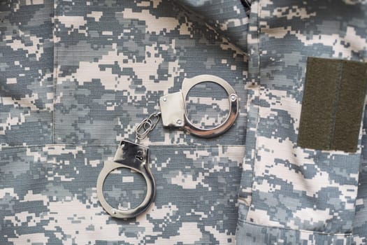 Handcuffs on a Camouflage background. Metal shackles isolated. Law. Limitation. Freedom. Security. Police bracelets. Military uniform. Soldier textiles. The texture of the spots. Camouflage colors