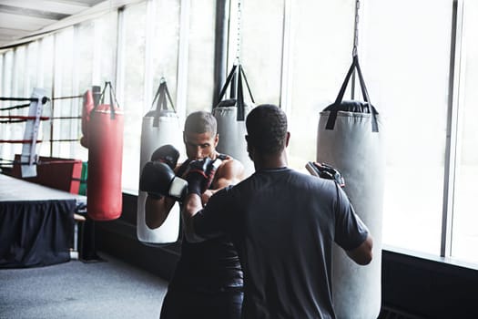 Preparing to be the greatest. a male boxer practising his moves with his coach.