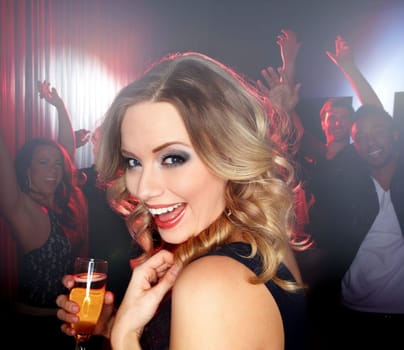 Feeling jovial. A lovely young blonde woman smiling at the camera while standing on the dancefloor holding a glass of wine.