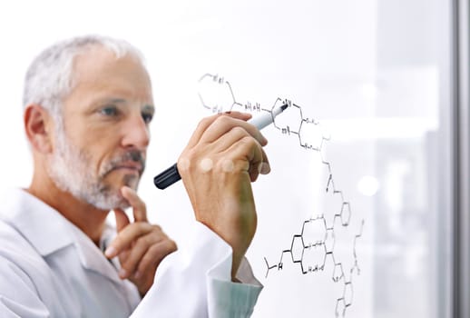 Hes doing some cutting edge research. a mature male scientist drawing a molecular structure on a glass surface.
