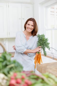 Crisp and fresh. A beautiful brunette holds a bunch of carrots while standing in her kitchen.