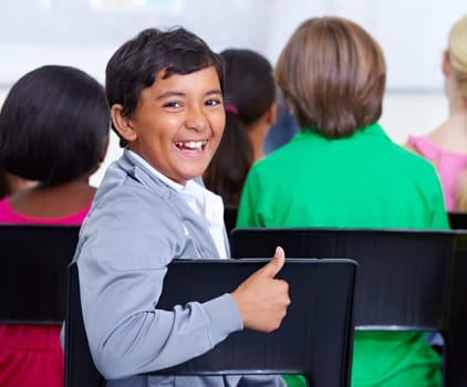 Eager young minds. Portrait of a young boy giving you the thumbs up while sitting in class.