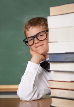 Exams No problem. A young boy wearing glasses and a bow-tie smiling at the camera from behind a stack of books.