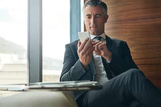 Technology keeps his workday organized. a mature businessman using his phone at work
