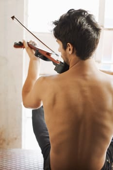 Back, music and a man playing the violin in his home while sitting shirtless as an artist or musician. Body, talent and instrument with a topless male violinist in rehearsal for a theatre performance