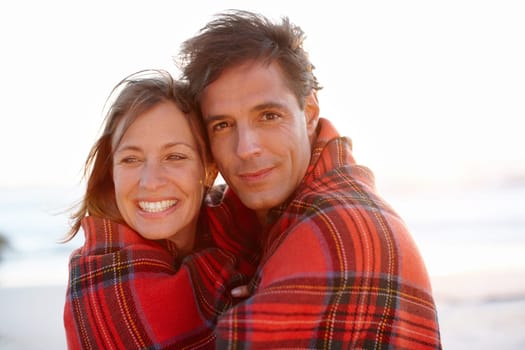 Wrapped up in romance. A devoted and affectionate couple wrapped in a blanket on the beach.