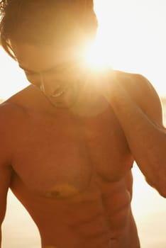 Basking in the sunlight. A handsome shirtless man smiling while standing outside with the sun behind him.