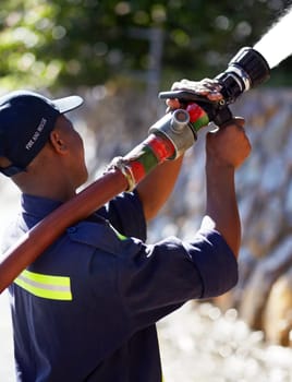 Firefighter man, water and spraying hose for emergency, rescue or firefighting services in the outdoors. Fireman using big liquid pressure pipe to spray down or put out fire outside for safety