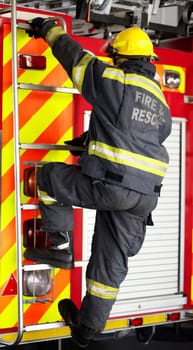 Firefighter, man and climbing ladder for emergency operation, service or rescue with equipment. Fireman person with helmet, jacket and gear protection getting on truck for firefighting at station